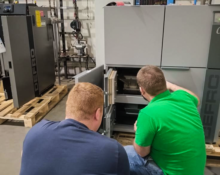 Twee technici inspecteren een open Defro-biomassaketel op de werkvloer